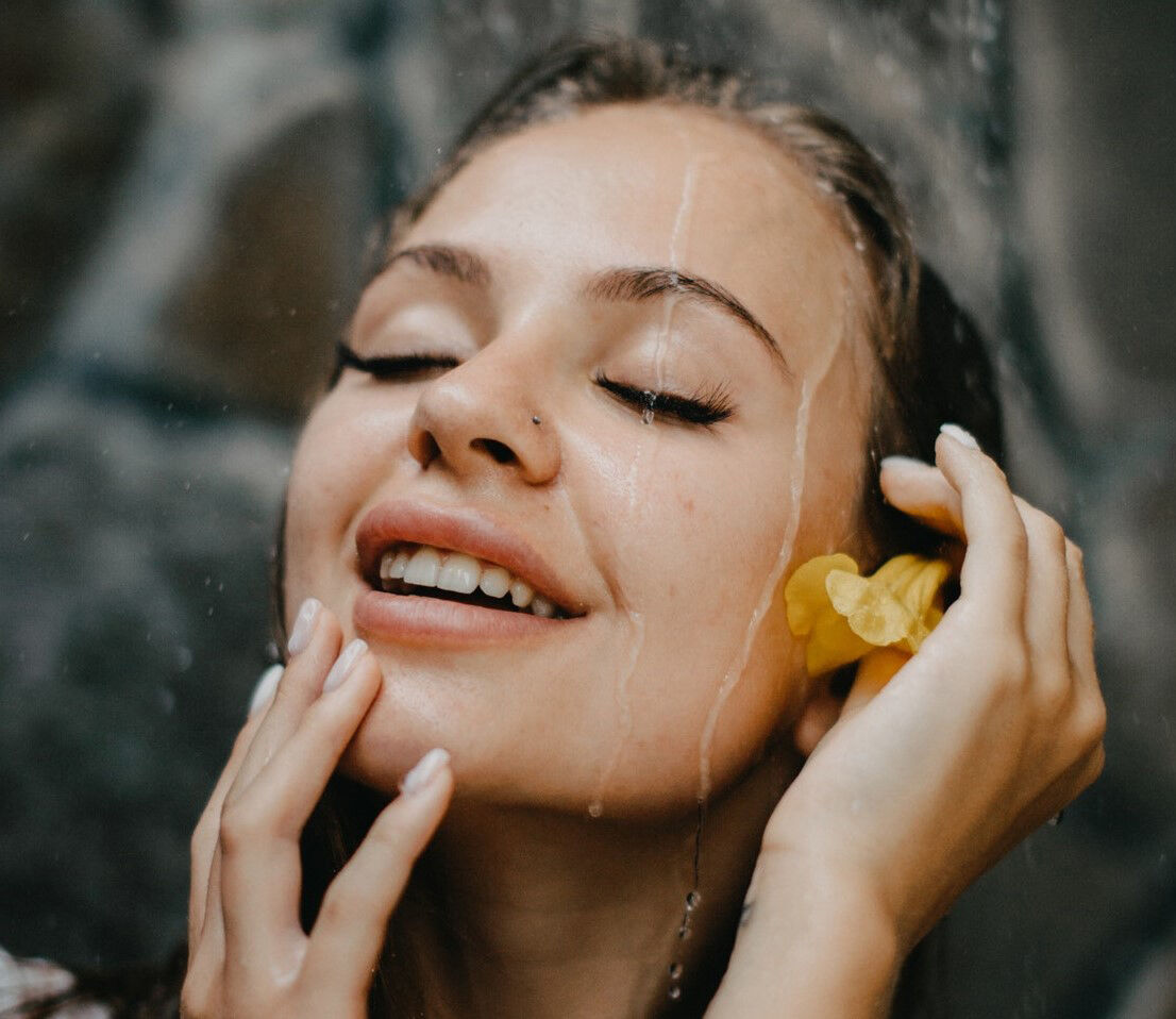 Happy woman feeling water on face during refreshing hair rinse.